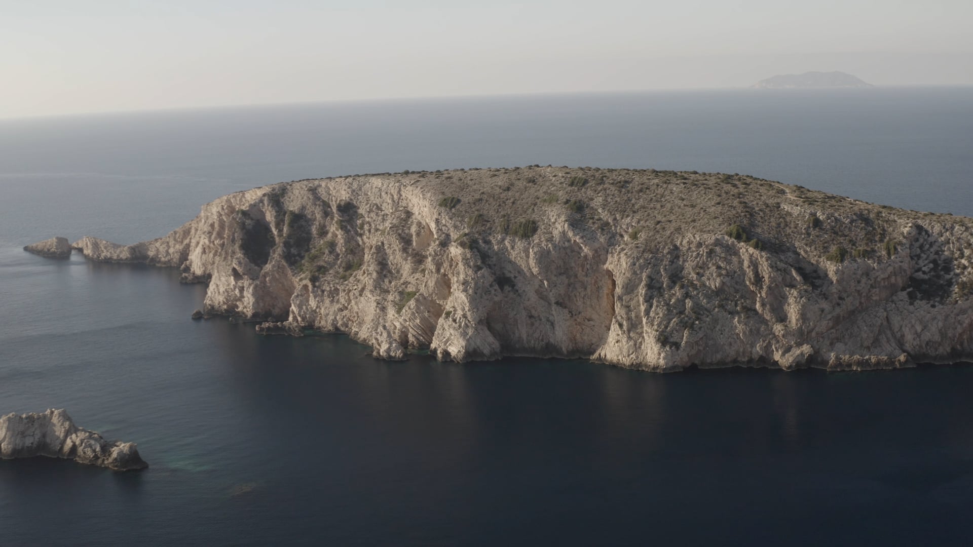 Rock island with few other islands visible, approaching the cave at the bottom of the cliff