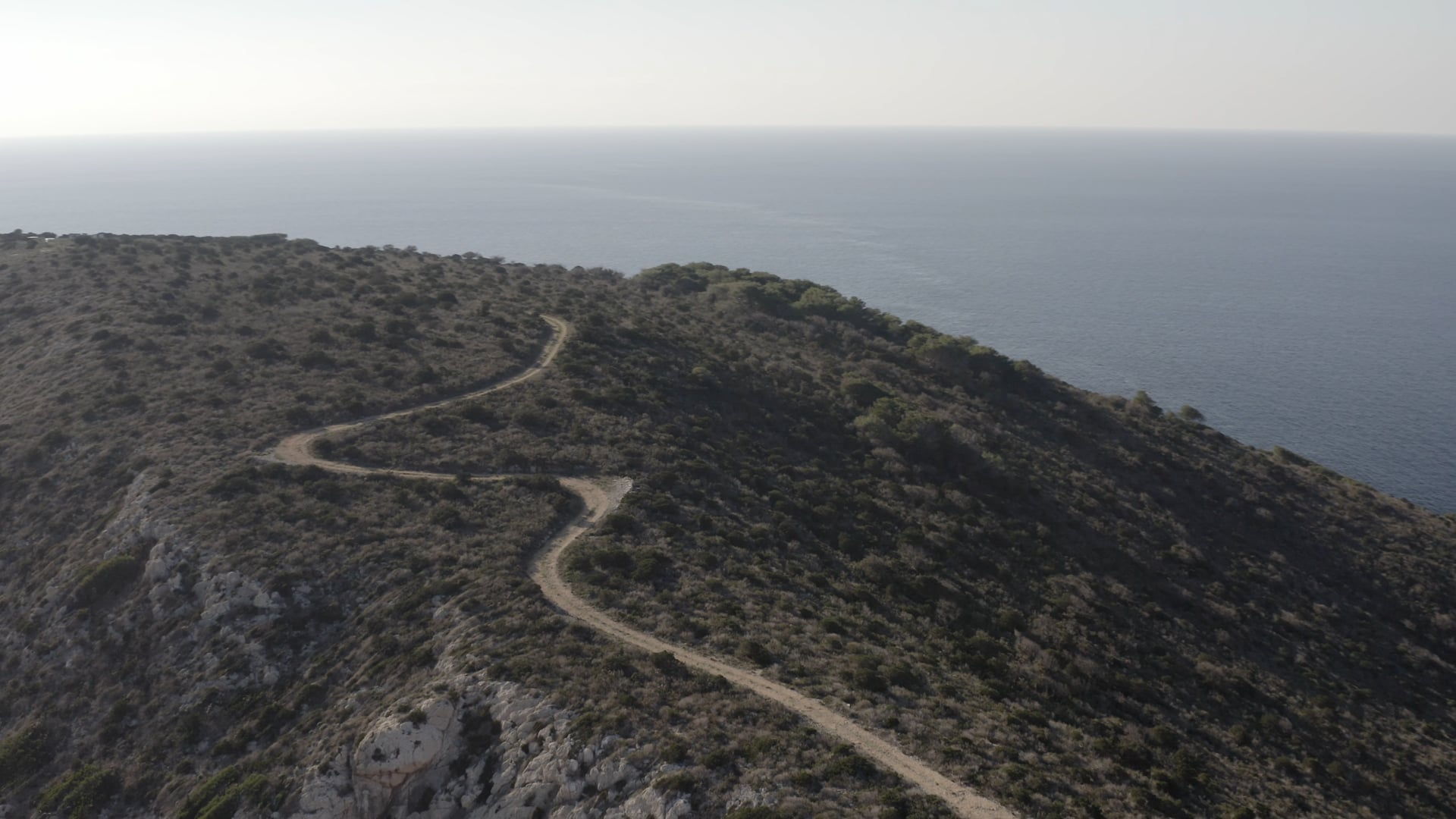Wavy road on top of the island, sun shining in the background