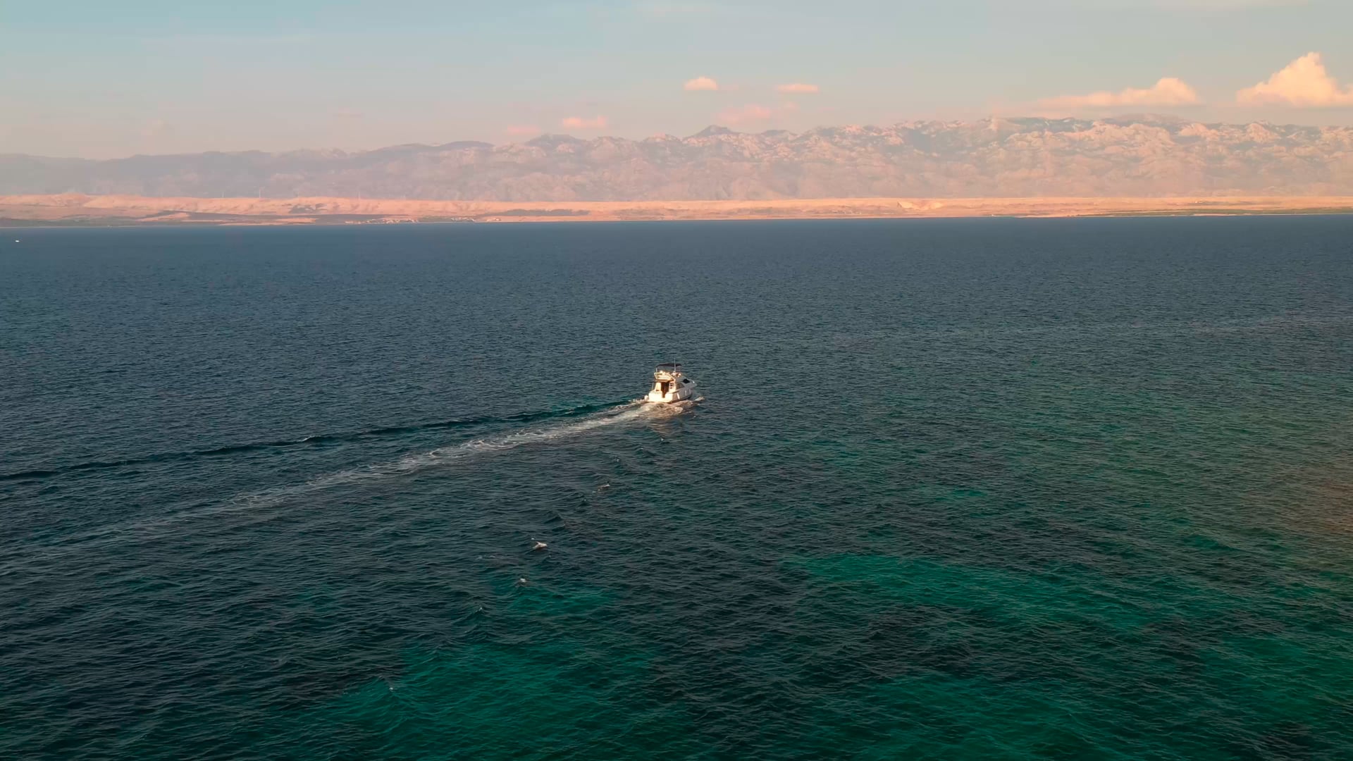 Small boat staying steady in the middle of the sea, mountain visible in the distance