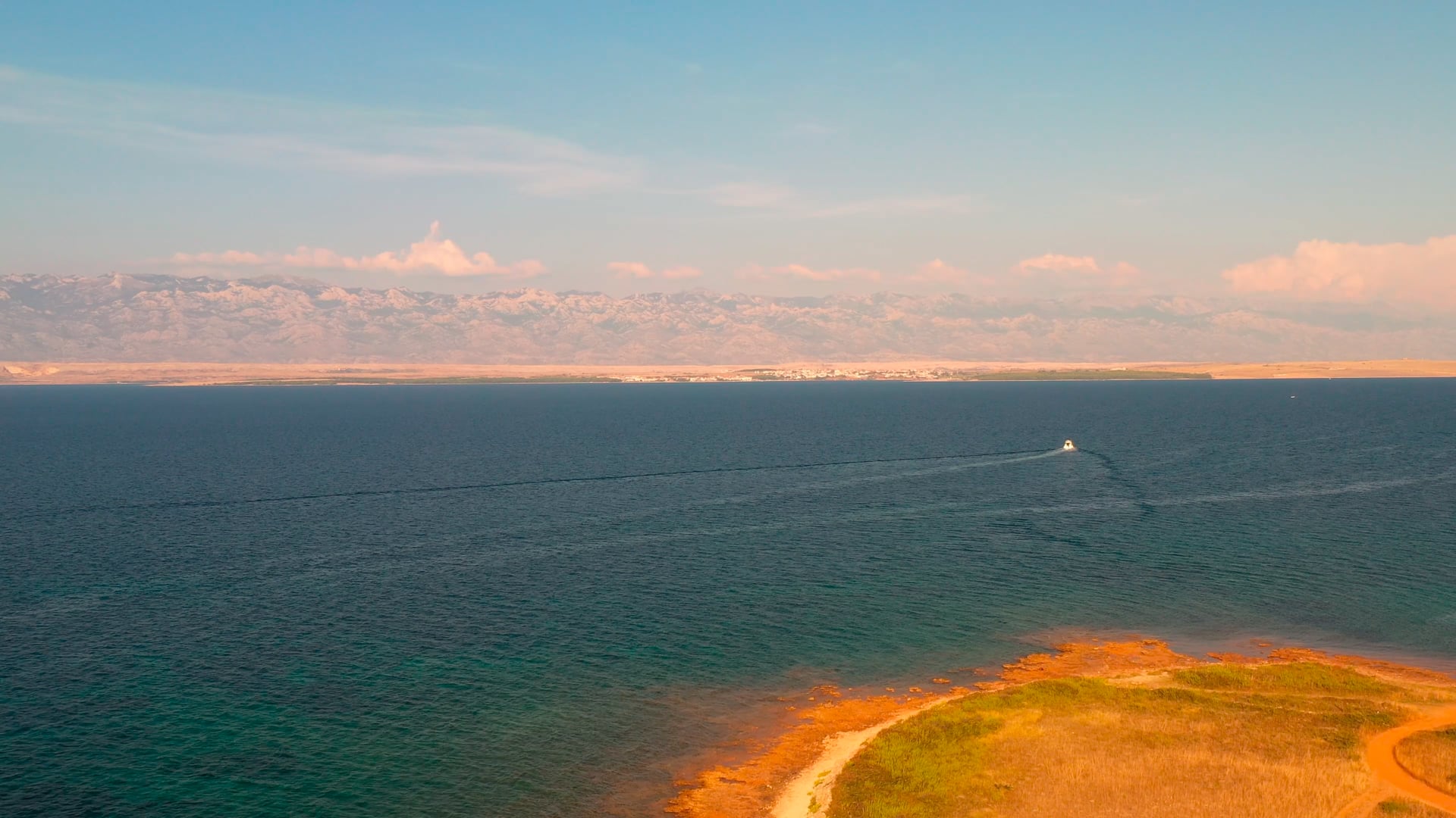 Boat sailing away from the coast, mountain and clouds visible in the distance