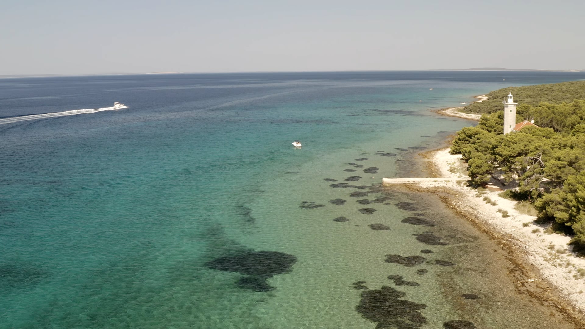 Boat sailing, panning to the lighthouse on the island coast, crystal clear light blue sea