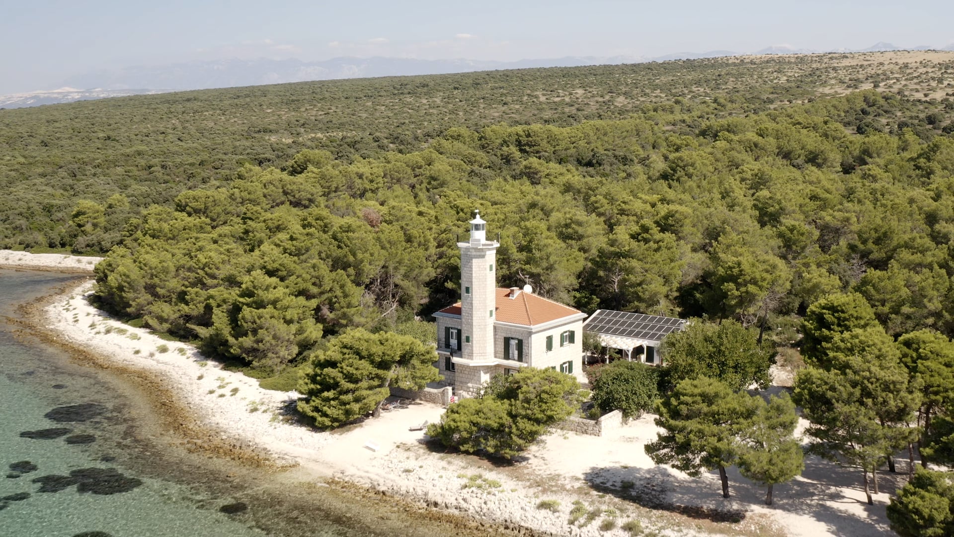 Forest and a lighthouse on the island coast, boats sailing in the distance