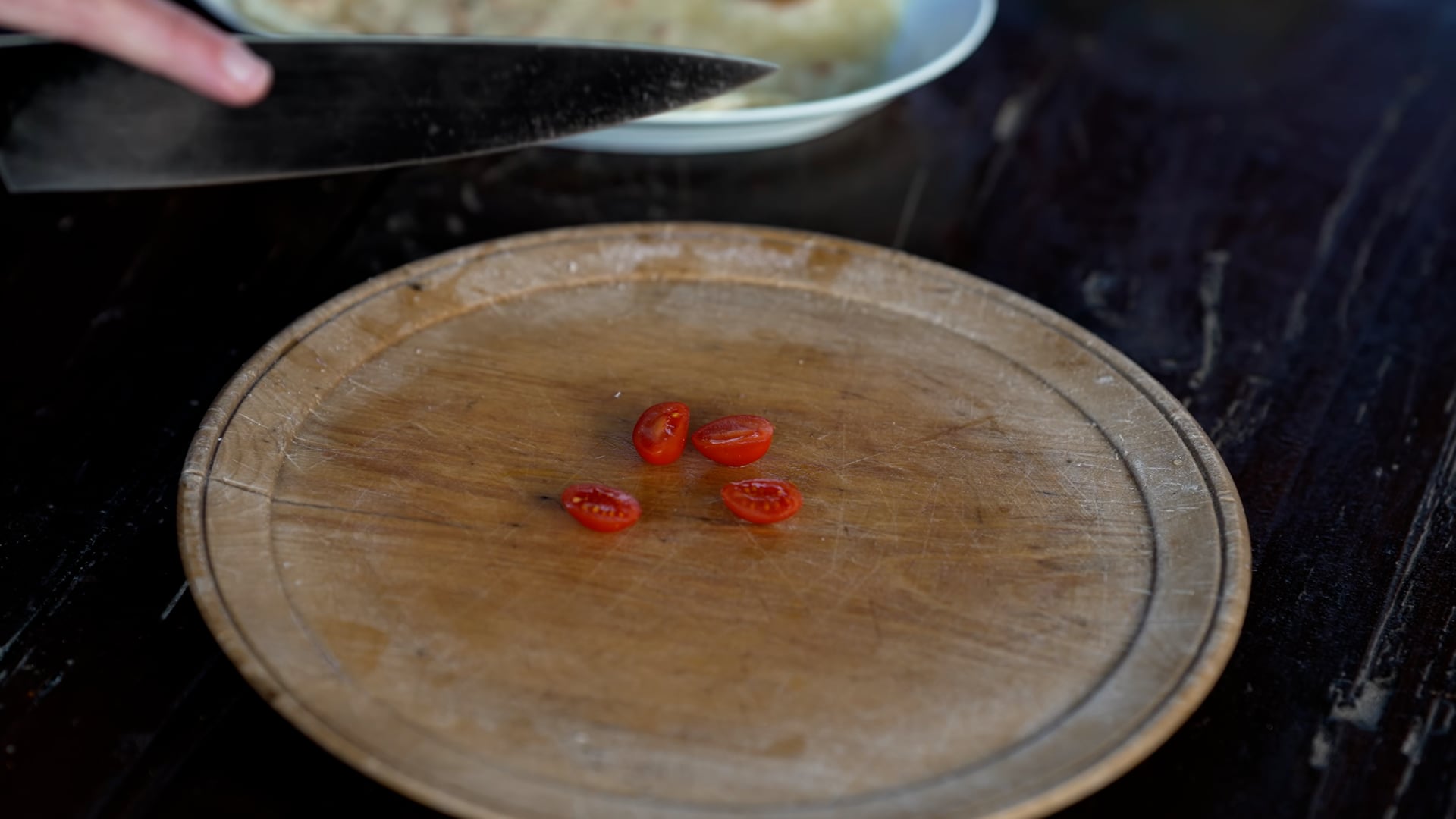 Cutting small tomatoes, zucchini and salad on the wooden plate with a big knife