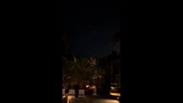A small light above trees and a lit restaurant patio in Desert Hot Springs.