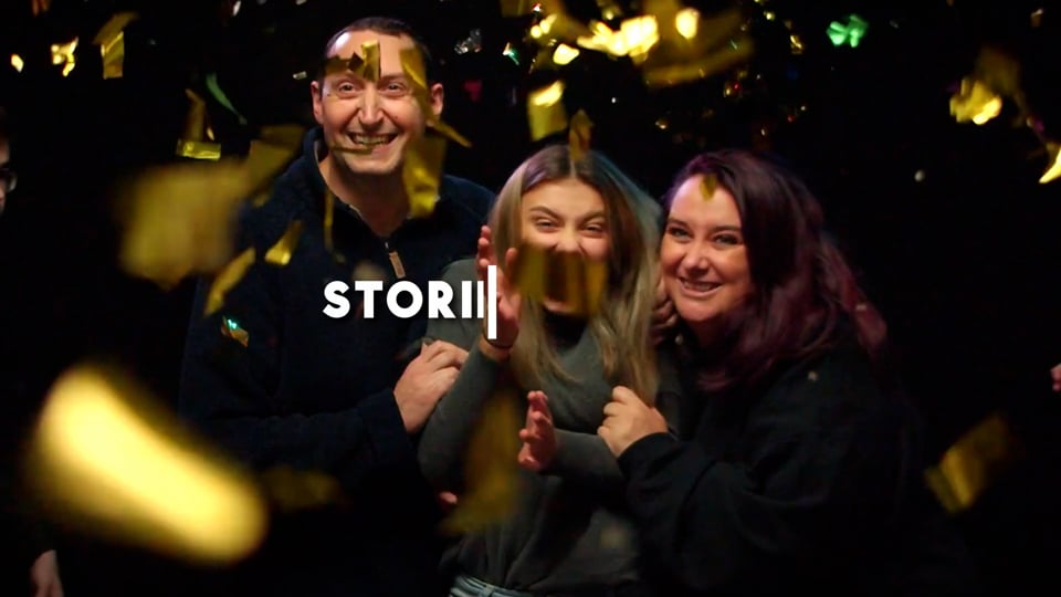 A young girl and her parents smiling and embracing infront of a black background with golden glitter falling around them.