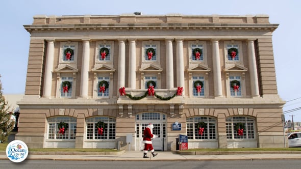 Santa walking in front of a building bearing Christmas decorations.