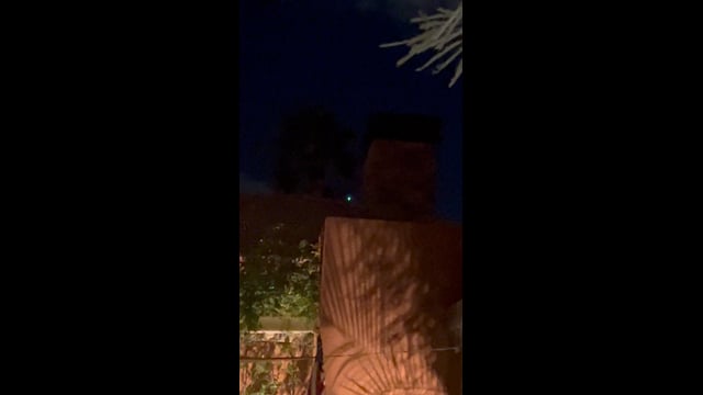 A blue-green light above a courtyard wall and roofline in La Quinta.