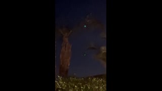 Two blue-green lights in the evening sky between palm trees in La Quinta.