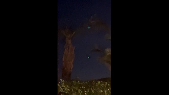 Two blue-green lights in the evening sky between palm trees in La Quinta.