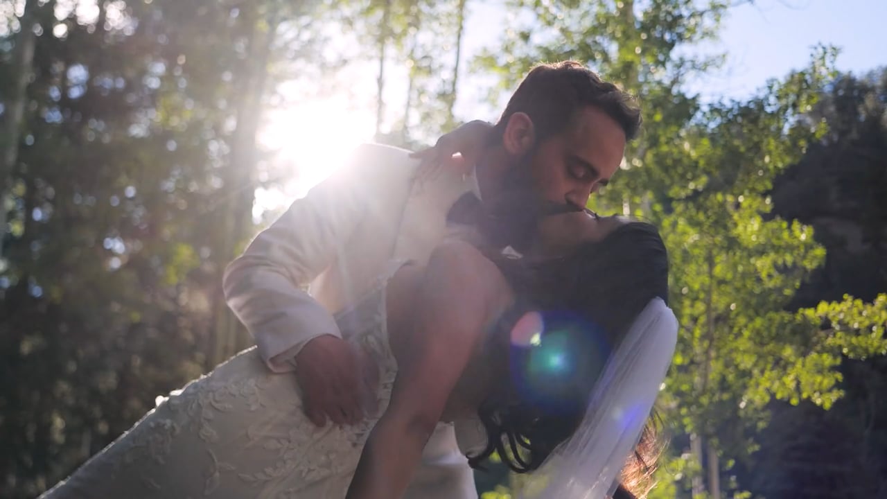 Valeria and Zach share a dip kiss under sunlit trees at Blackstone Rivers Ranch, with the sun flaring through the branches behind them