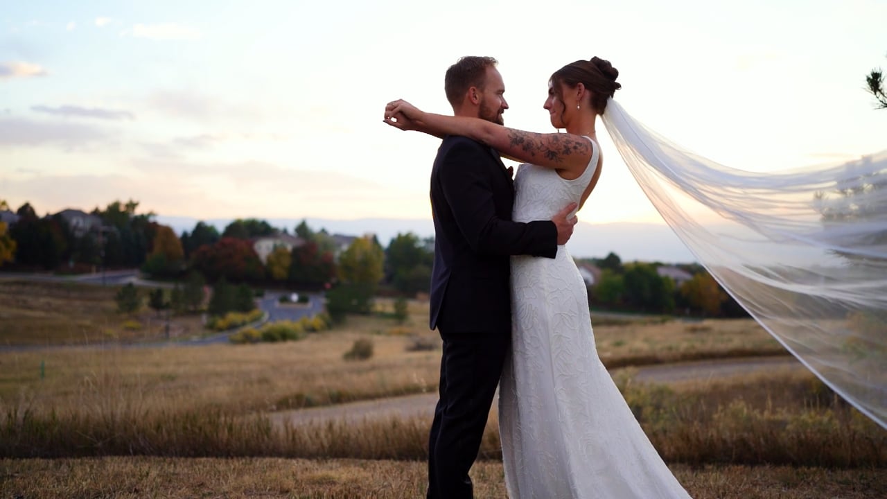 Courtney and Mark embrace on a grassy hill in Highlands Ranch at sunset while her long veil blows out behind them