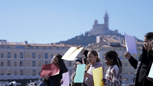 Manifête : deuxième étape     Après les ateliers pour définir les thématiques de cette grande manifestation, les élèves sont partis explorer le parcours Manifête accompagné·es de la scénographe Alice Ruffini ! Où leur regard se pose-t-il ? Que remarquent-i·els dans l'espace qui les entoure ? Un repérage à hauteur d’enfants où ils et elles ont également pu tester différents éléments de scénographie : dessin à grande échelle, écriture de slogans sur du tissu et jeux de couleurs.    Manifête  Rendez-vous le 12 juin 2025 en ouverture du 30e Festival de Marseille    © Louison M. Vendassi et Camille D. Tonnerre