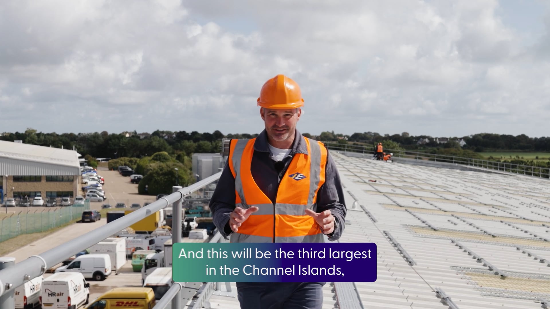A person standing on an industrial roof wearing an orange high-vis jacket and hard hat.