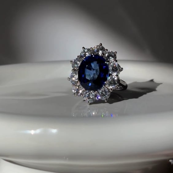 4.5ct Oval Cut Center sapphire surrounded by 12 Round Cut Stones of 2.5 TCW. Center stone size: 12x10mm F233-SAP-CZ-14K