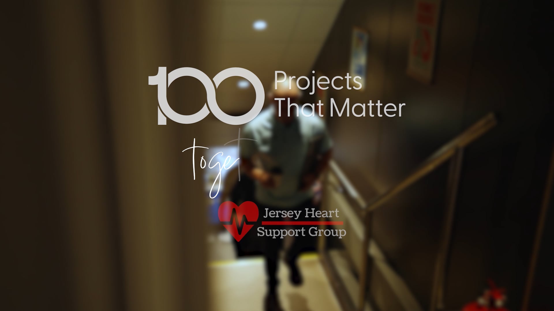 A person wearing a blue jumping, smiling and sat at a table in front of a laptop