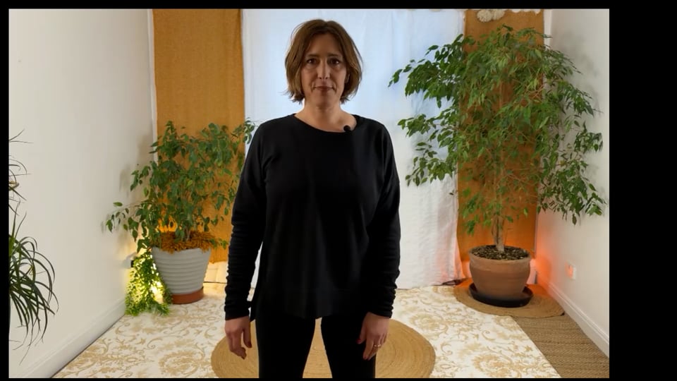Online Qigong teacher standing calmly in a home studio, introducing what Qigong is.