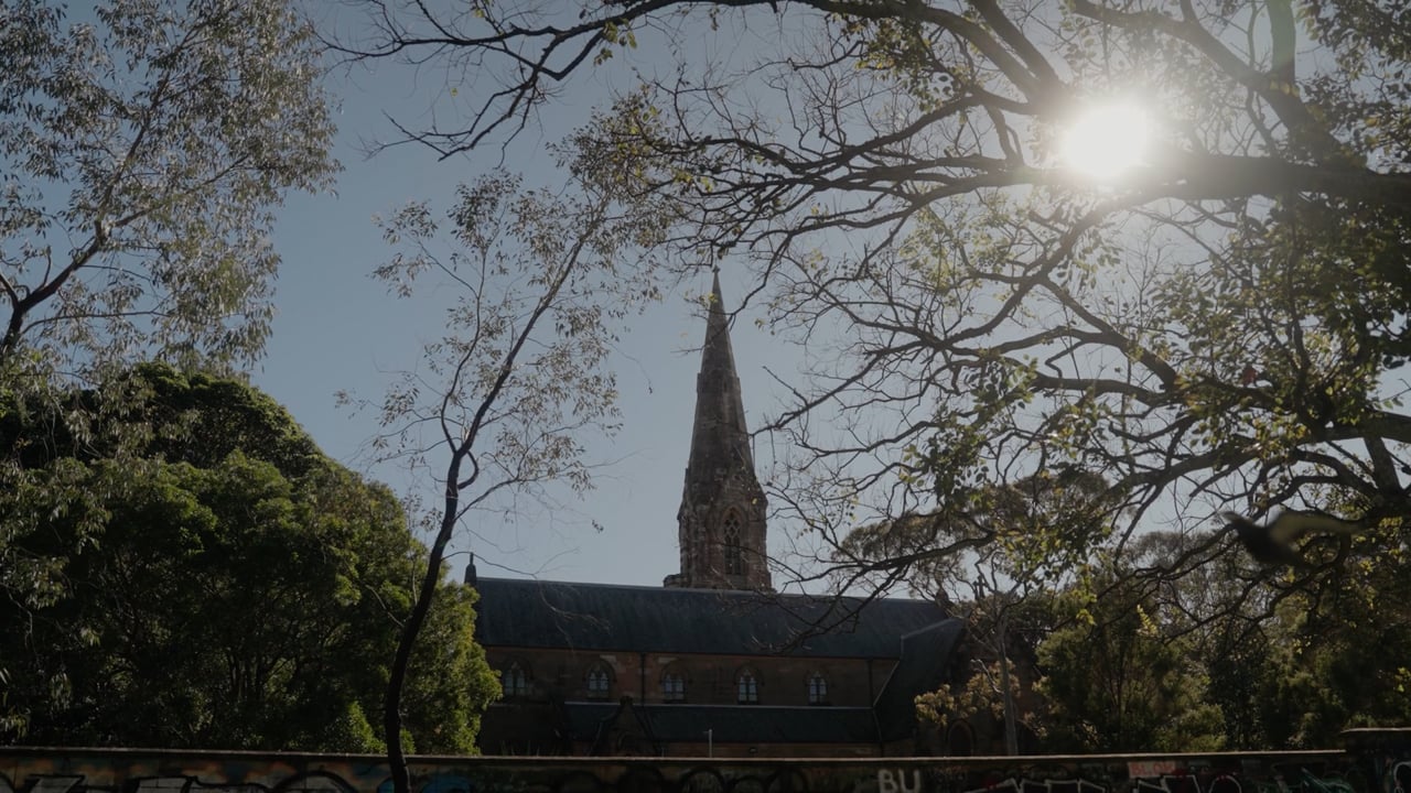 A sandstone church and its spire seen through trees, from the CCCAust national identity film