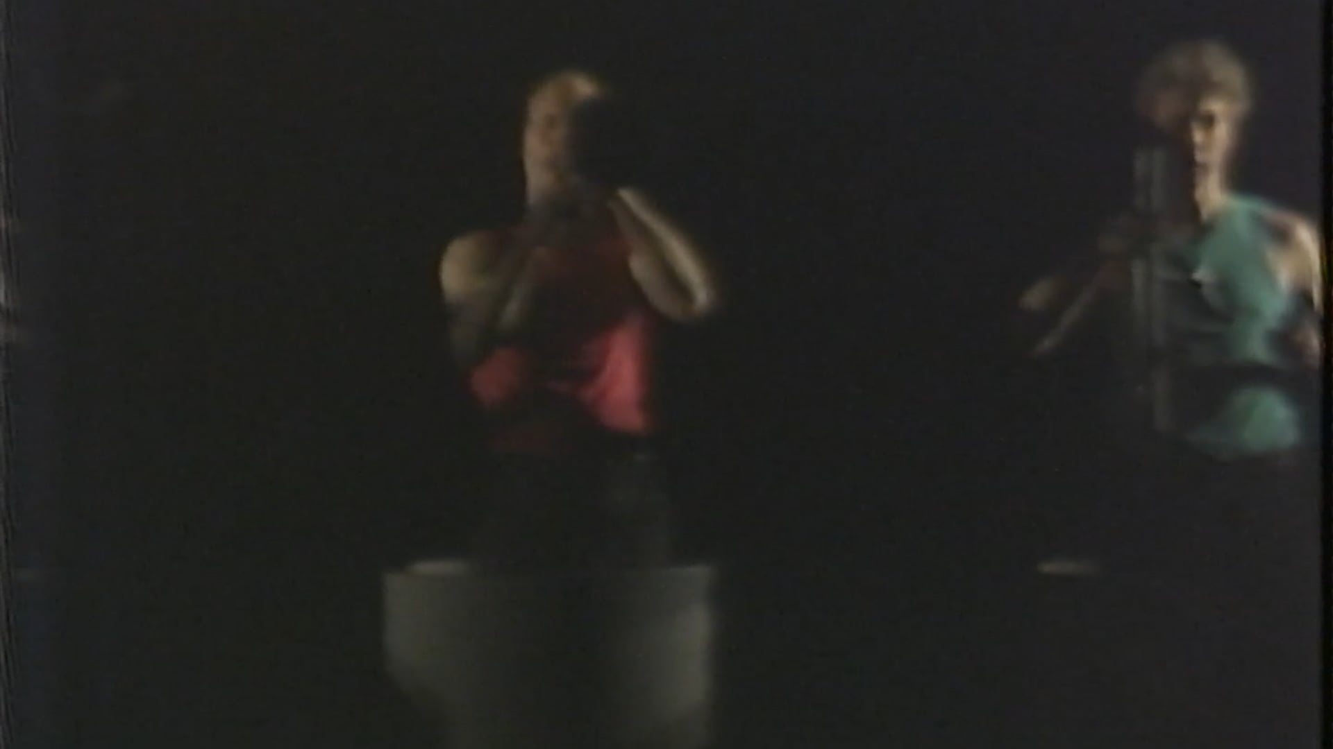 Are Are premiered at Theatre Artaud’s Cavernous Performance Space in San Francisco in March 1983. The second part of the “How Trilogy,” it reunited Paul Dresher, Rinde Eckert, John Duykers, and Leonard Pitt, shifting from the distinct individual figures of The Way of How toward a coordinated group identity.
The performance opened with three performers hunched behind rear-lit screens, appearing as indistinct forms before emerging to measure their bodies with retractable tapes. Set on a deep, runway-like stage, the work developed around repeated attempts to measure, rise, and overcome physical limits. The performers moved in rolling barrels, climbed onto a rolling piano, appeared on stilts, and ultimately ascended in block-and-tackle harnesses with arms extended in flight. Pink and green projected patterns covered the performers as they rose. Through these successive scenes, Are Are developed a theme of ascent: the performers pool their efforts, negotiate gravity, and finally achieve lift-off