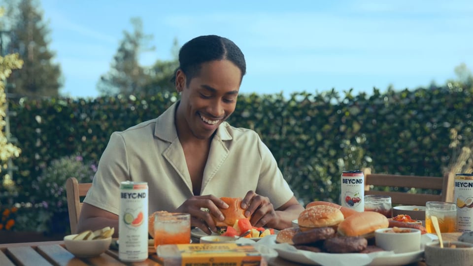 Man smiling while eating a burger outdoors, surrounded by Beyond Meat products