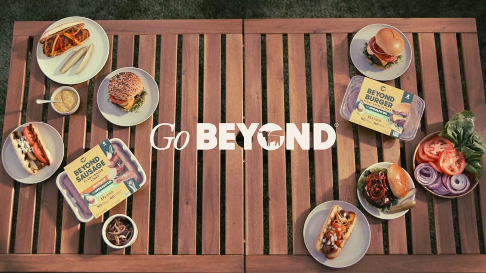 Overhead shot of burgers, hot dogs, and Beyond Sausage packaging on a wood table