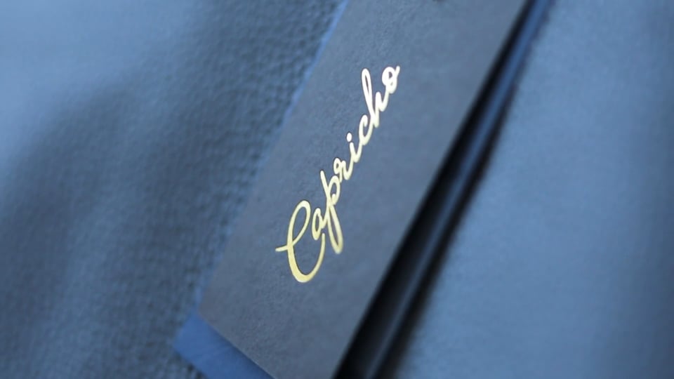 Close-up of dark packaging with a gold foil Capricho script logo