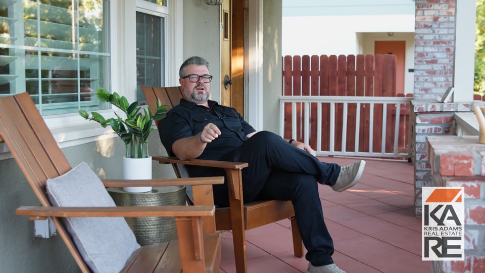 Man being interviewed while seated on a porch, for a Kris Adams Real Estate video