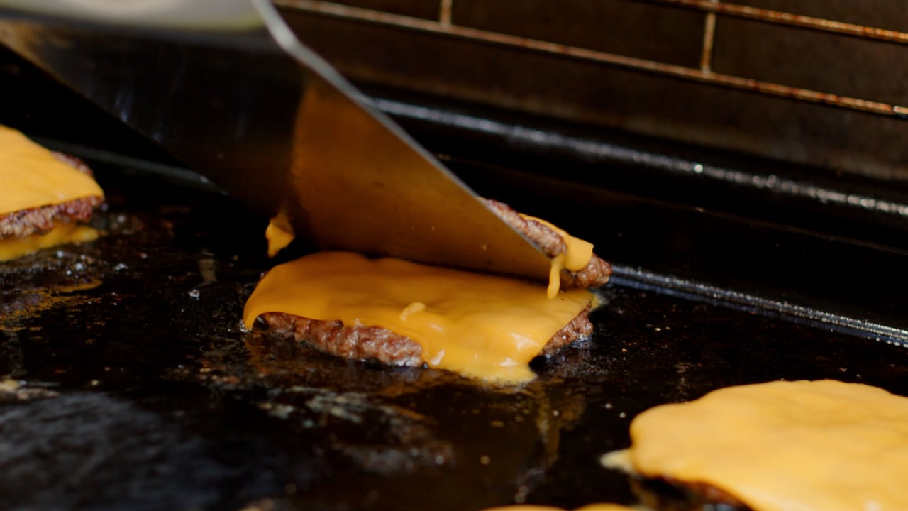 Showreel poster frame: the spatula lifting a smash burger off the griddle, cheese pulling