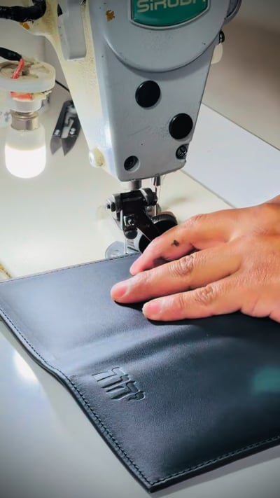 Hands guiding a dark tract folio cover through a sewing machine in the Ministry Ideaz workshop