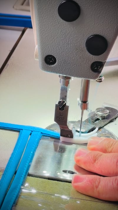 Hands sewing turquoise fabric edging onto a clear tract organizer in the Ministry Ideaz workshop