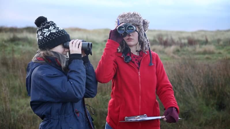 Video screen cap: two students using binoculars