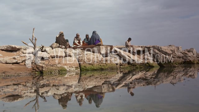 Boy Sits Near Adults At Edge Of River