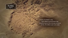 Satellite image of the Tin Bider Crater. A gray box in the top left corner has text that reads "Tin Bider, Algeria." Text at right reads "A lack of rainfall in this high desert environment has helped preserve the intricate terraces of this 70-million-year-old crater."