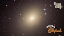 Image of an elliptical galaxy. A scroll graphic in the top right corner has text that reads "Galaxy Types." White and brown text in the bottom right corner reads "Enormous Ellipticals."