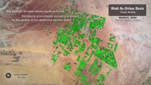 Satellite image of irrigated areas in Saudi Arabia. A gray box in the top right corner has text that reads "Wadi As-Sirhan Basin, Saudia Arabia." A light gray box is just below that reads "March, 2000. Thematic Mapper, Landsat 5." A gray circle in the bottom left corner has the letter "N" and an arrow pointing toward the top. On its right is a small gray bar that is labeled "10 km." Text in the top left corner reads "The addition of water allows plants to thrive. Increasing groundwater pumping is shown by the spread of the distinctive circular fields."