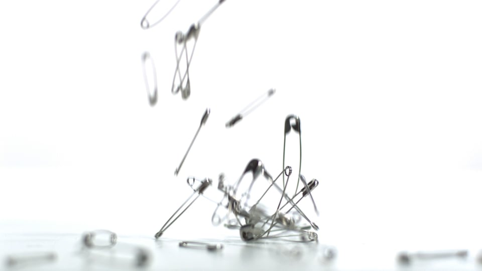 Safety pins falling on white background Video from Pikwizard