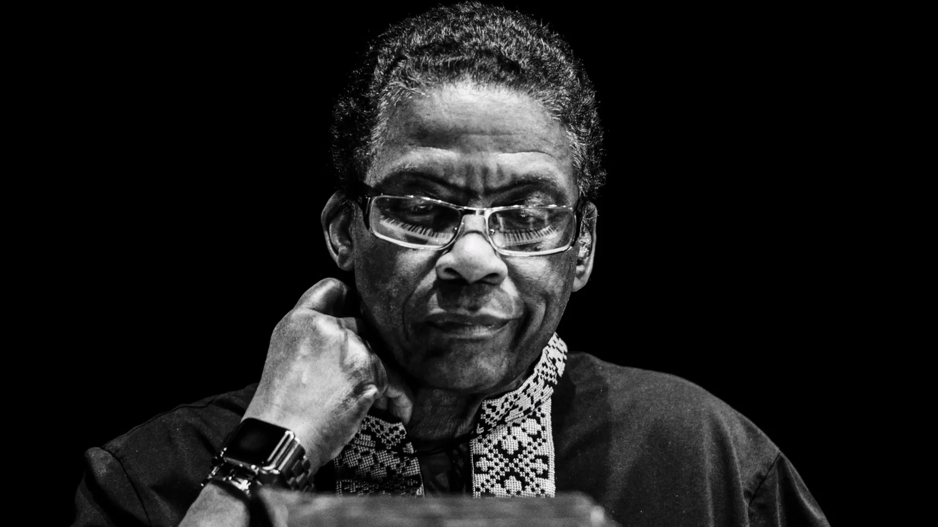 Black-and-white portrait of Herbie Hancock wearing glasses, with one hand resting against his neck.